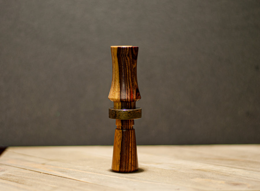 Cocobolo duck call showing contrasting wood grain and a patinated metal band
